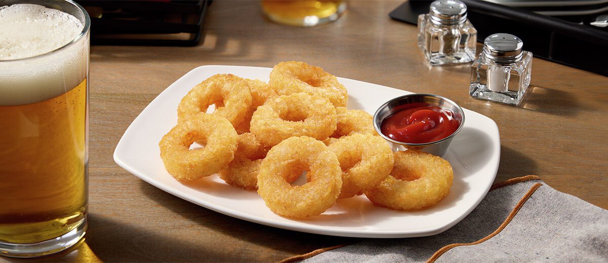 potato rings on a white plate next to a beverage