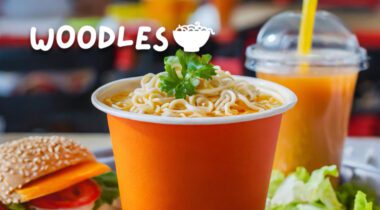 orange paper cup full of cooked noodles with parsley on top. Woodles logo over