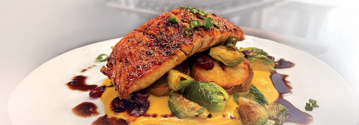 plated salmon dish with brussels sprouts, cranberries, potatoes and orange soy glaze on white plate