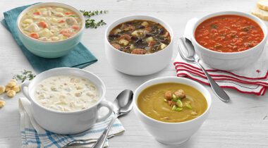 5 bowls of various soups on napkins, on a white table