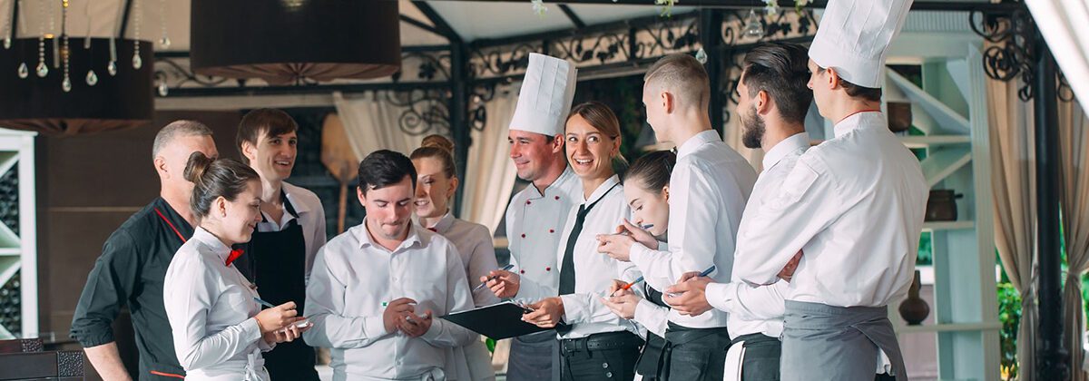 10 men and women wearing white and black standing around a kitchen island for a meeting