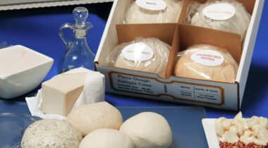 Box of 4 pizza dough balls next to opened dough balls and plate of garlic and seasoning