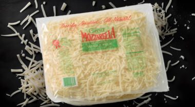 Sealed bag of shredded mozzarella cheese over cheese shreds on black table