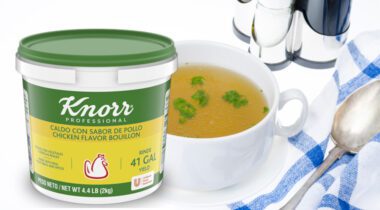 container of Knorr Chicken Flavor Bouillon over soup cup of prepared chicken stock next to napkin, soup spoon