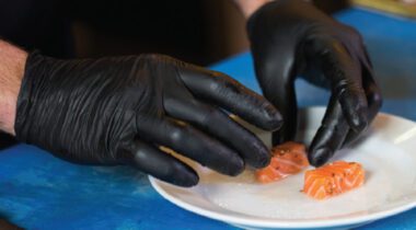 male hands wearing black gloves preparing fish on white plate