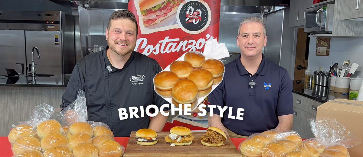 2 smiling people at a table of buns rolls with graphic text says brioche style with signs and marketing for Costanzo's bakery