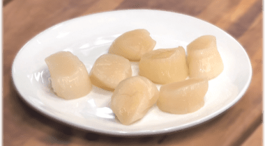 7 raw scallops on a white plate on wood