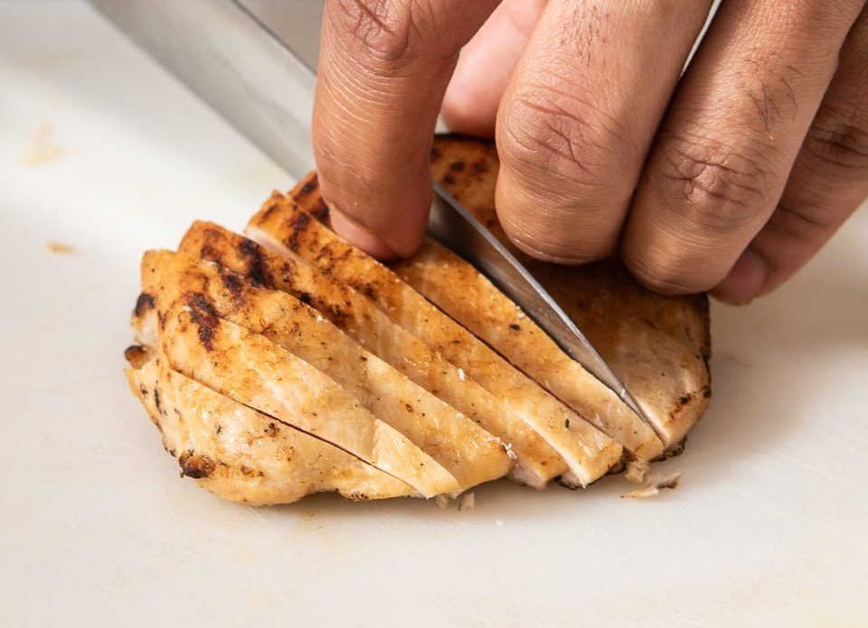 hand holding and slicing chicken breast