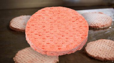 frozen iqf burger patty, pathed, in front of other patties on a griddle