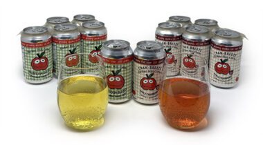 glasses of sparkling cider, one yellow, one pink, flanked by 12oz cans with cute apple labels