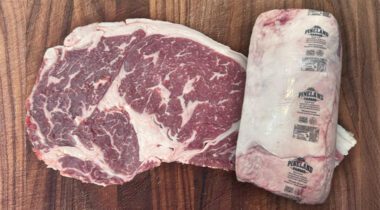 a raw ribeye steak behind a seal ribeye primal
