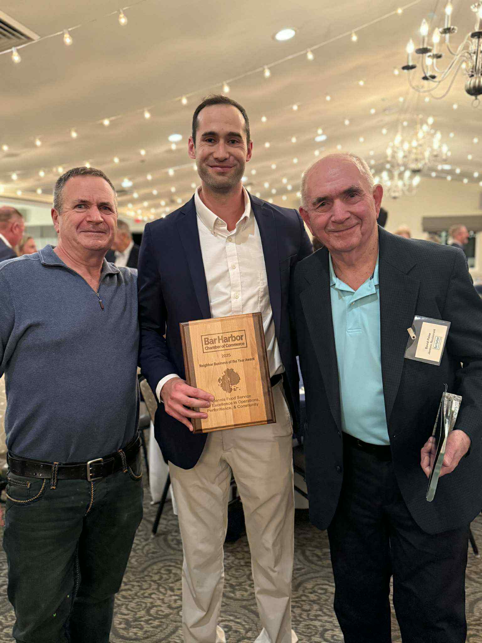 threee men pose for a photo at a white tent event, the middle man has an award