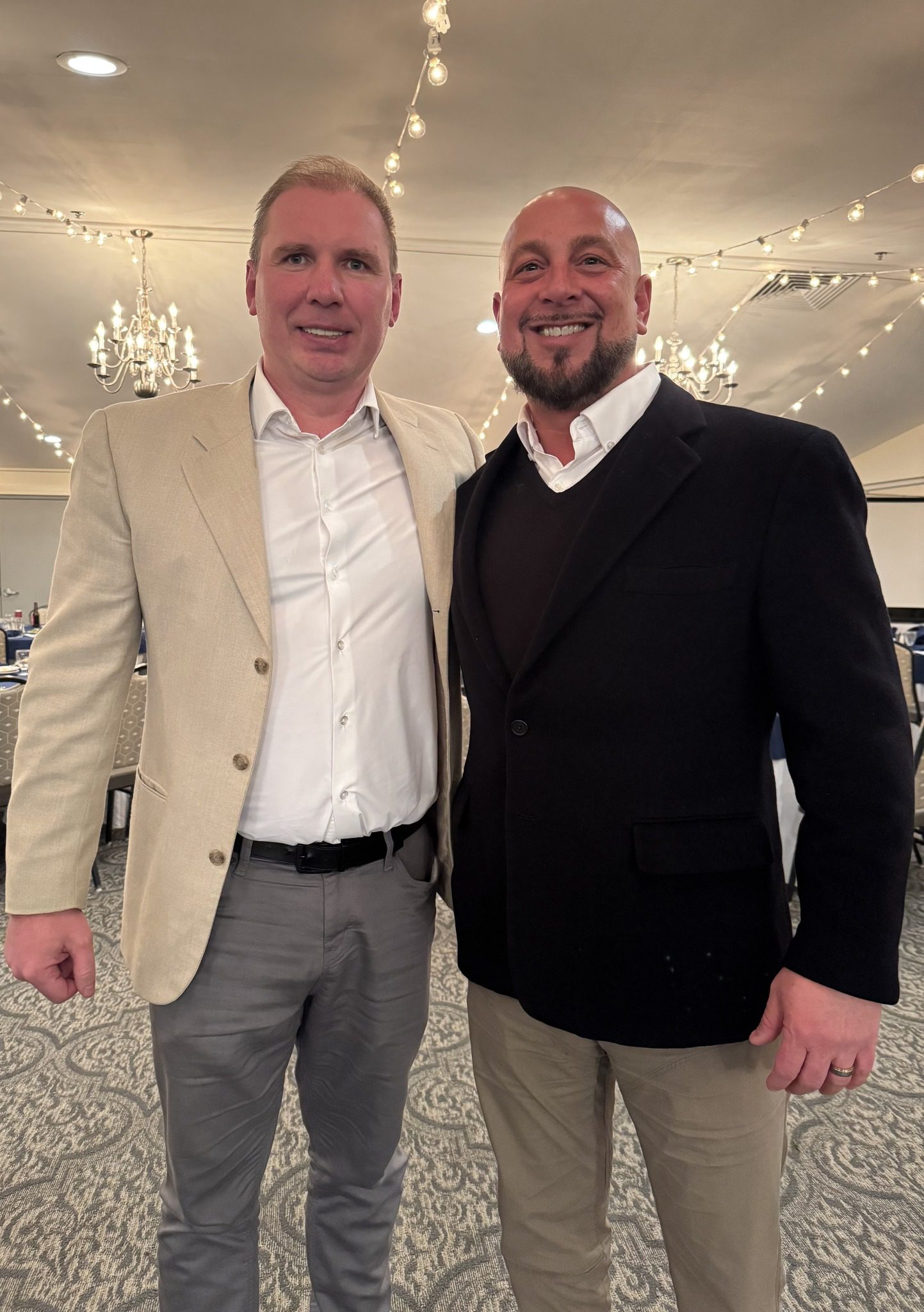 two men pose for a photo at a white tent event