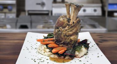 pork shank plated with carrots and greens in a kitchen