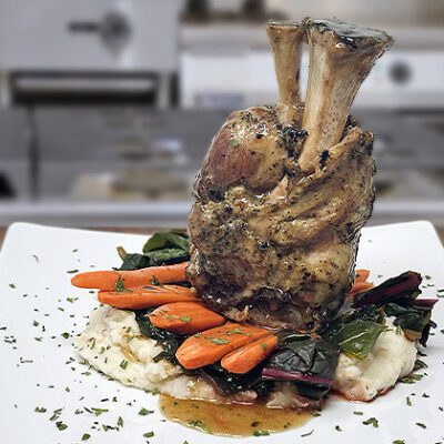 pork shank plated with carrots and greens in a kitchen