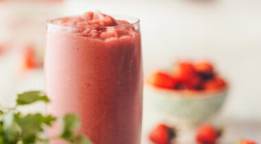 glass of frozen strawberry smoothie with blurry bowl of strawberries in background