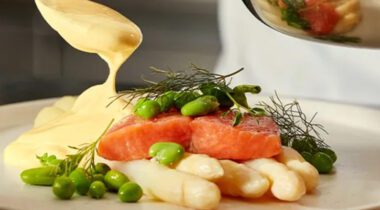 hollandaise sauce being spooned onto a salmon and veggies