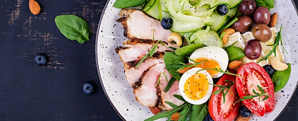 a top down shot of a plate of sliced pork, salad, eggs, nuts and olives