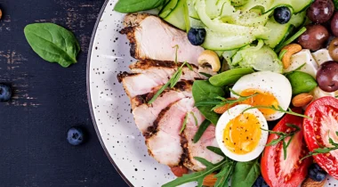 a top down shot of a plate of sliced pork, salad, eggs, nuts and olives