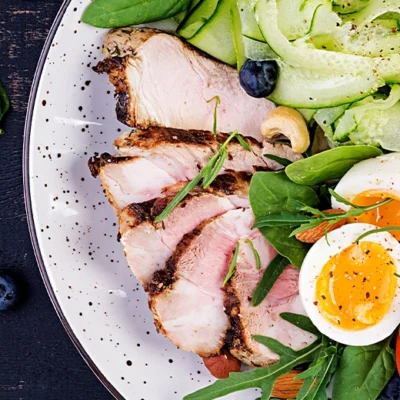 a top down shot of a plate of sliced pork, salad, eggs, nuts and olives