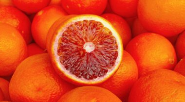 cut orange with bright red interior ontop of whole oranges