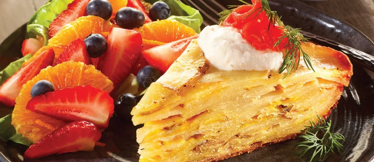 Potato Torta topped with Smoked Salmon and a side of fruit salad on a gray stoneware plate