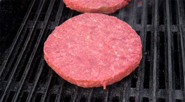 raw beef burger patty on a grill