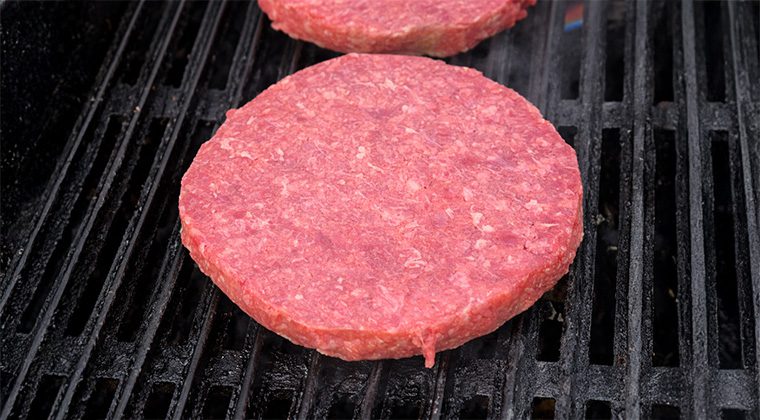 raw beef burger patty on a grill