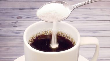 cup of black coffee with sugar being poured from spoon into coffee