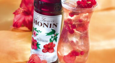 bottle of Monin Hibiscus drink flavor next to glass of sparkling berry drink