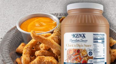 gallon of Ken's Chick'n Dip'n Sauce over plate of a fried appetizer and cup of orange dipping sauce