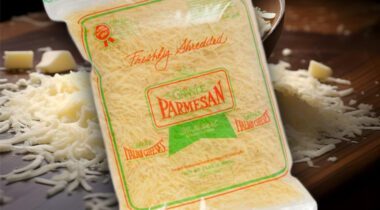 closed bag of shredded Parmesan cheese over Grated cheese on a wooden board.