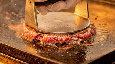 Gloved Hand Pressing Raw Beef Smash Burger on Hot Griddle Close Up