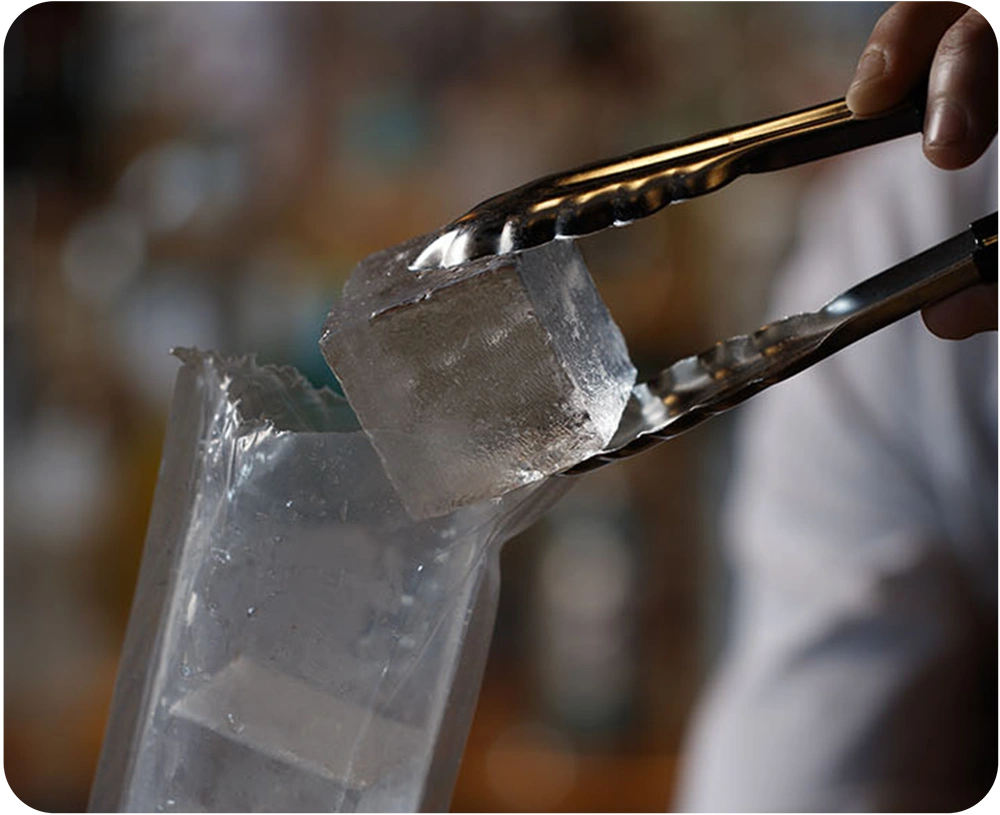 square ice cube held in tongs, removed from a plastic sleeve of perfect ice cubes