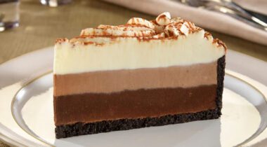White plate with a slice of 3 layer chocolate torte and oreo cookie crust.