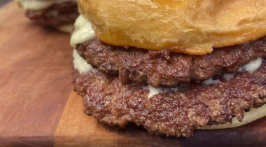 double cheese burger with crisp thin burger patties sticking out from bun, white cheese