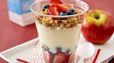 clear plastic cup filled with strawberries, blueberries, yogurt and granola
