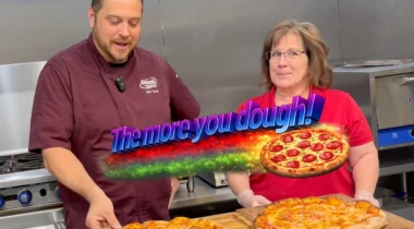 The More You Dough graphic image, logo over 2 people with pizzas in stainless steel kitchen