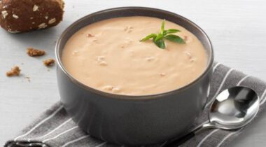 gray bowl, soup spoon, napkin place setting with red-orange creamy soup (lobster bisque)