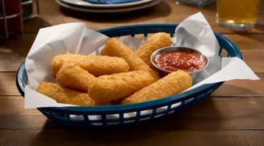 battered cheese sticks in a serving basket with parchment paper and a ramekin of marinara